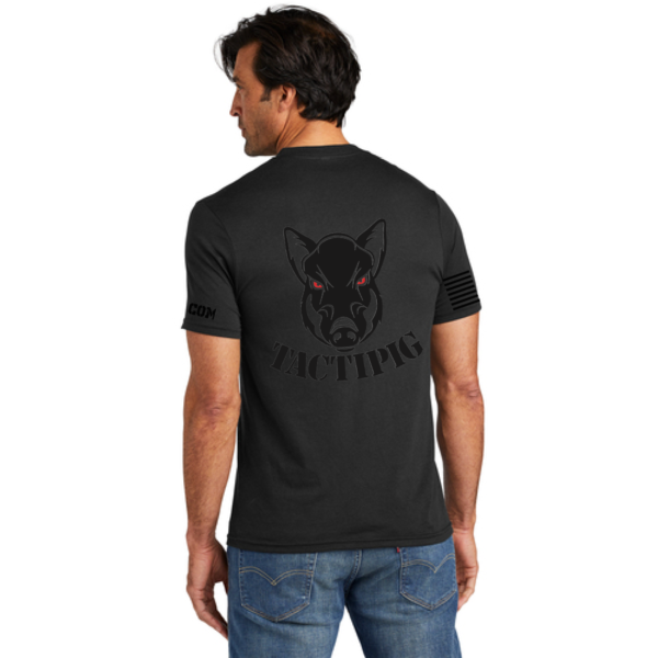 Back view of a man wearing a black Tactipig t-shirt featuring a large boar head logo with red eyes and the word "TACTIPIG," along with an American flag design on the sleeves.